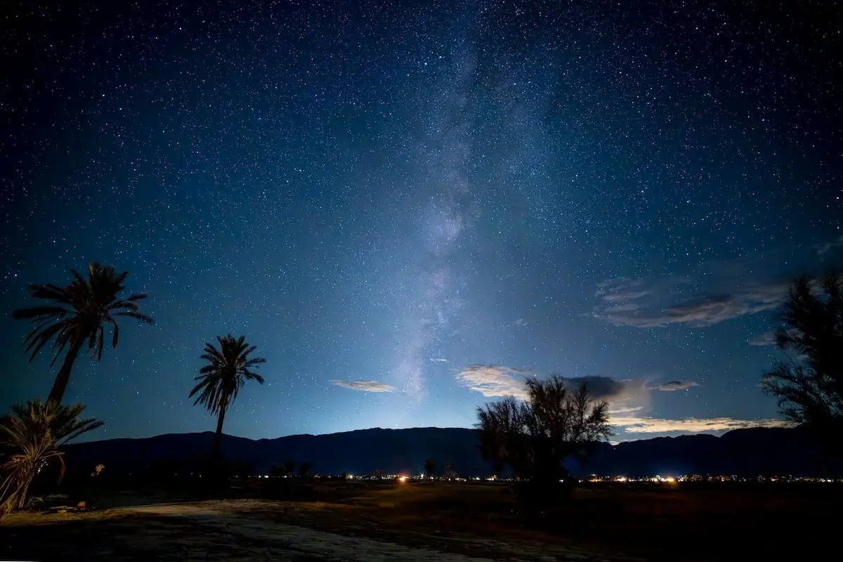 Deep star-filled sky with the light from the sun barely visible over the mountains