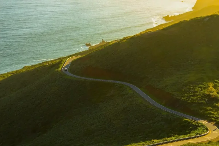 Aerial view of a winding road through green hills with the ocean to the left