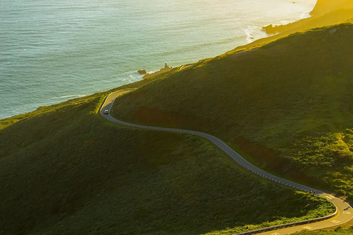 Aerial view of a winding road through green hills with the ocean to the left