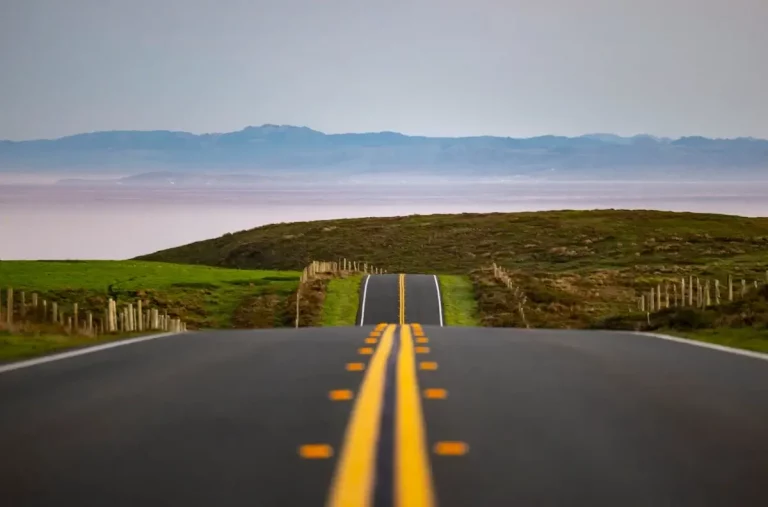 Two-lane highway running through fields with mountains in the background