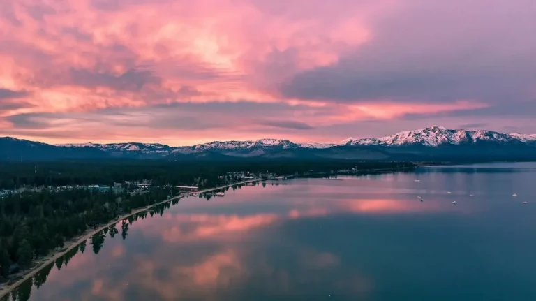 A soft pink sunset over the west shore of Lake Tahoe with snow-caped mountains in the distance