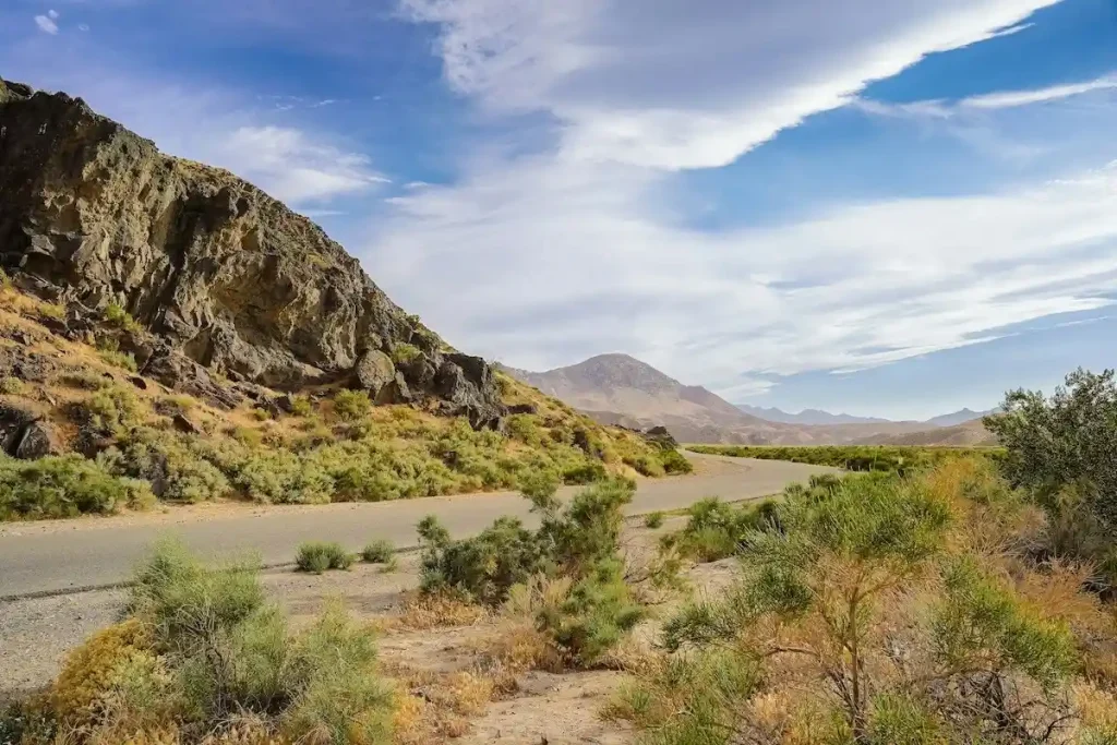 Single-lane road twisting around a mountain in the Mojave desert with green brush