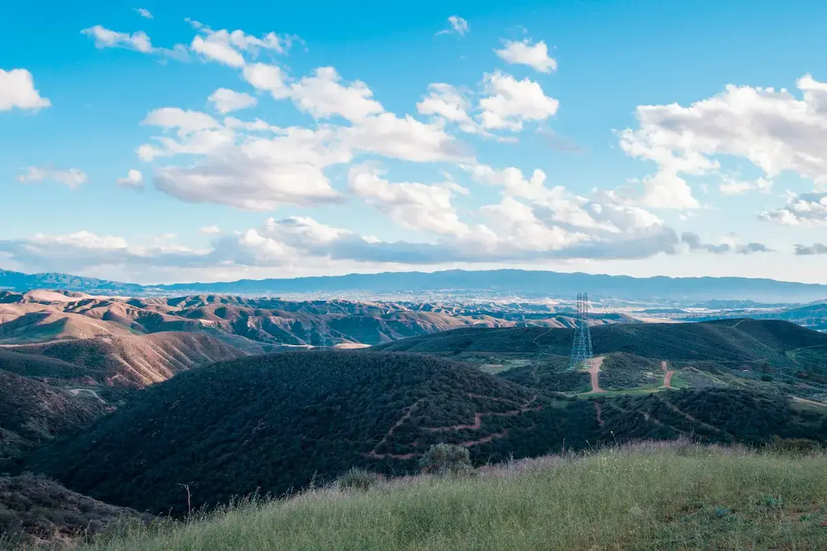 Aerial view over green rolling hills wit bright blue cloud-filled sky